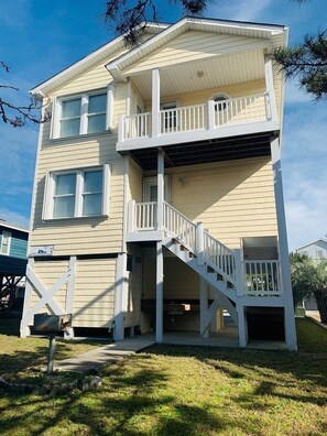A two-story building with a balcony on the upper floor, a staircase leading to the entrance, and a small porch area. - Sandy Toes 3 Bedroom Home by RedAwning (Supply)