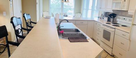 A kitchen with a long island, white cabinets, a microwave, stove, and a hanging light fixture.