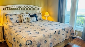 A bedroom with a bed, a nightstand, a lamp, and a view of the outdoors.