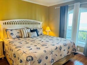 A bedroom with a bed, a nightstand, a lamp, and a view of the outdoors.