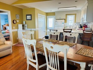 A dining area with a wooden table, white chairs, and a kitchen in the background.