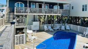 A two-story house with a balcony, a pool, and a deck with lounge chairs.