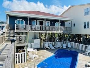 Uma casa de dois andares com varanda, piscina e um deck com cadeiras de descanso.