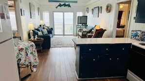 Una cocina amplia con una isla central, un comedor con mesa y sillas, y una sala de estar con sofá y televisor.