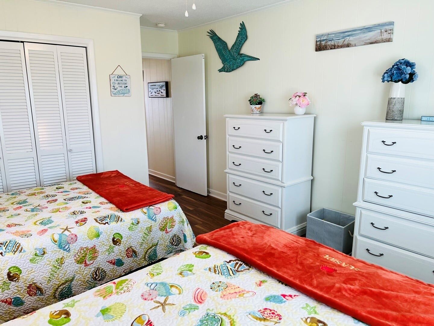 Un dormitorio con dos camas, un aparador, un adorno de pájaro en la pared y una puerta que da a otra habitación.