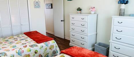 Un dormitorio con dos camas, un aparador, un adorno de pájaro en la pared y una puerta que da a otra habitación.