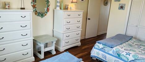 Un dormitorio con cama, cómoda, mesita de noche, espejo y puerta.