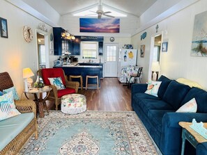 A cozy living room with a blue sofa, a red armchair, a wicker chair, a small round ottoman, and a patterned rug.
