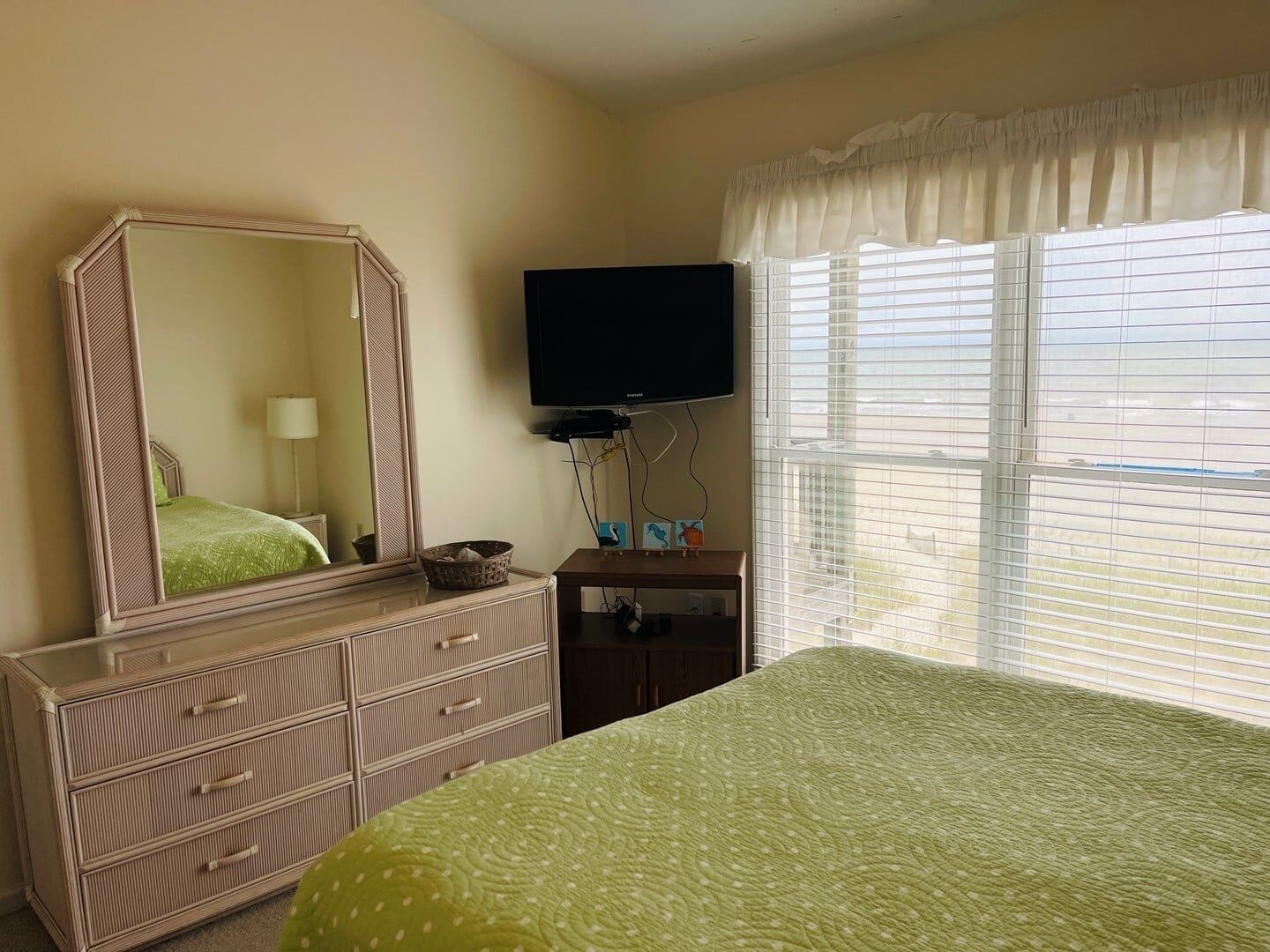 A hotel room with a bed, dresser, TV, and window with blinds.