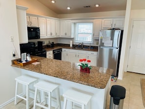 A kitchen with white cabinets, granite countertops, a stainless steel refrigerator, and a window. - Serenitee - 2 Br Home (Supply)