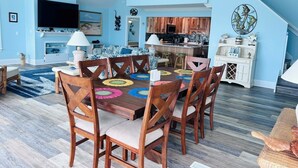 A dining area with a wooden table and chairs, a television, and a kitchen in the background. - Serenity's Star 4 Bedroom Home by RedAwning (Supply)