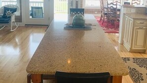 A kitchen with a granite countertop, wooden chairs, and a hanging light fixture. - Shore Beats Workin' 5 Bedroom Home by RedAwning (Supply)