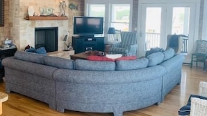 A spacious living room with a large gray sectional sofa, a flat-screen TV, a fireplace, and a ceiling fan. - Shore Beats Workin' 5 Bedroom Home by RedAwning (Supply)