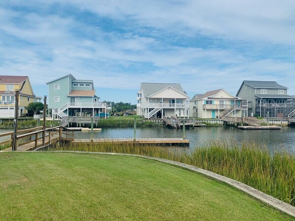 A waterfront property with multiple houses connected by docks, a grassy area in the foreground, and a clear sky.