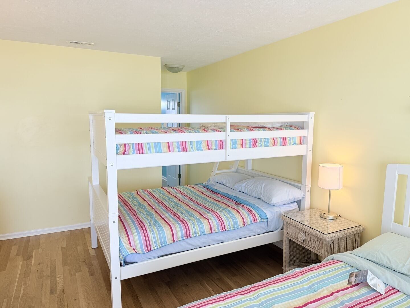 Ein Stockbett mit gestreifter Bettwäsche, eine Nachttischlampe und ein Weidenbeistelltisch.