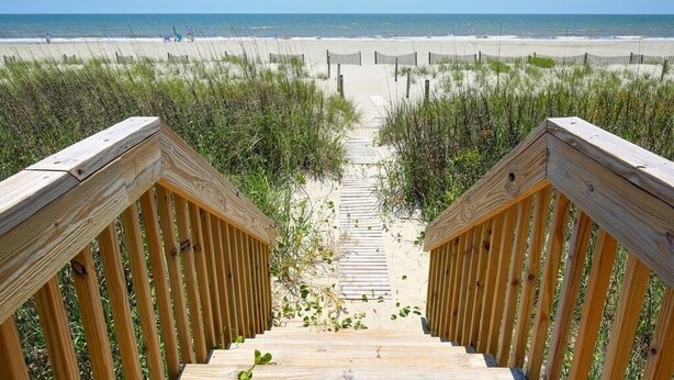 A wooden staircase leading to a beach with a clear view of the ocean.