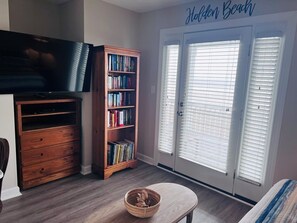 A room with a bookshelf, a television, a door with blinds, and a small table with a basket.