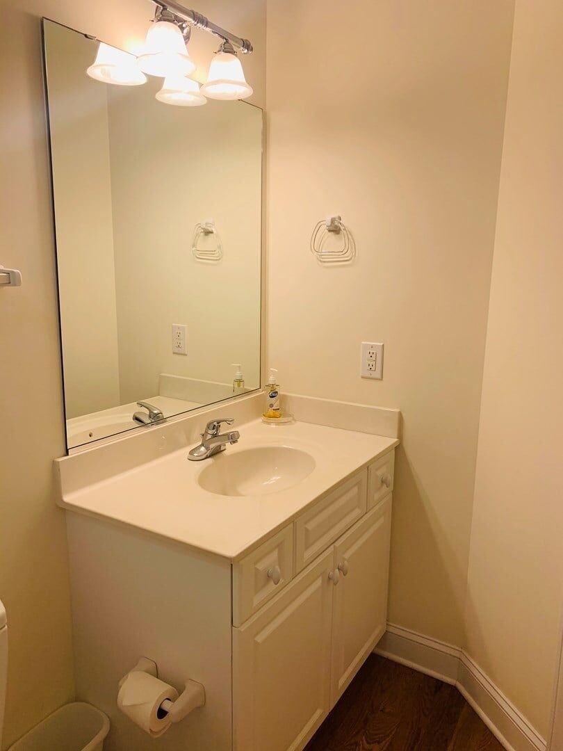 Un bagno con un lavandino bianco, uno specchio, un portascopino e un water.