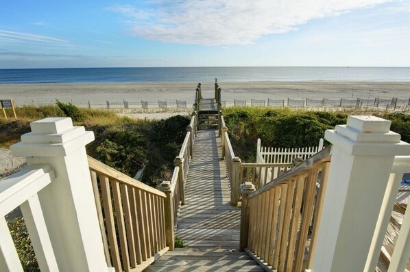 A wooden staircase leading to a beach with a white fence on either side.