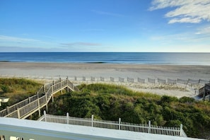 A beach with a wooden staircase leading down to the shore, a white fence, and a clear sky.