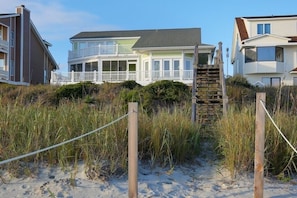 A beachfront property with a two-story house, a covered porch, and a wooden staircase leading to the beach.