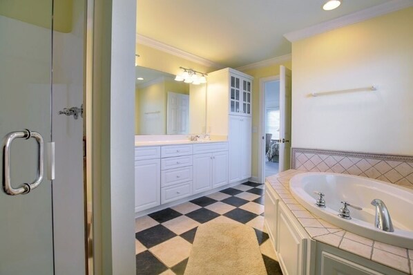 Un baño con piso a cuadros, una bañera grande y muebles blancos.