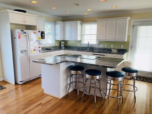A kitchen with white cabinets, a granite countertop, a built-in island with bar stools, and a refrigerator with magnets. - Sweet Dreams Private  4 Bedroom Home by RedAwning (Supply)