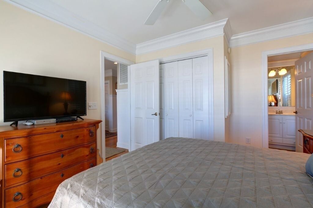 A bedroom with a bed, a dresser, a television, and a closet.