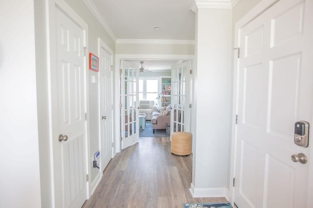 A hallway with white doors, a basket, and a view into a living area with a sofa and bookshelves.