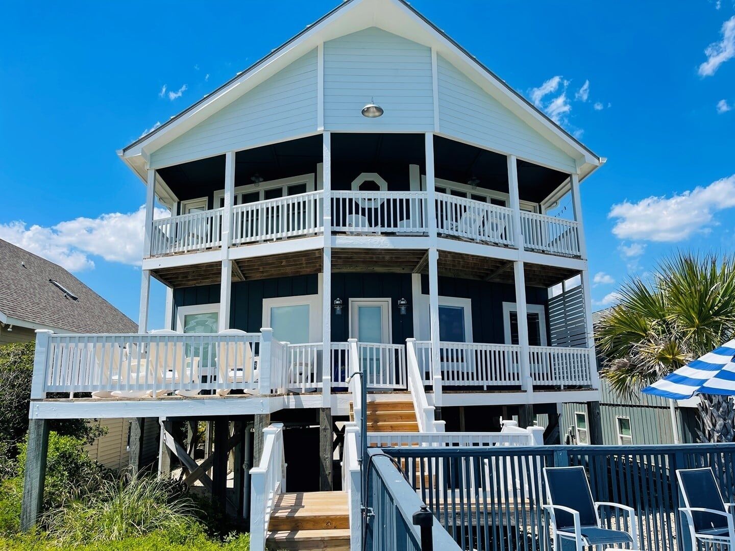 Une maison de deux étages située en bord de mer, dotée d’un balcon, d’une terrasse en bois et d’un espace salon extérieur.
