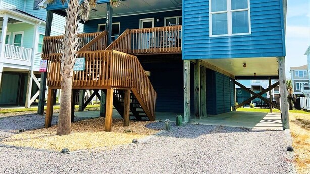 A two-story house with a wooden deck, a palm tree, and a clear sky.
