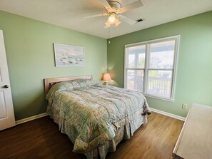 A bedroom with a bed, a ceiling fan, a window, and a painting on the wall.