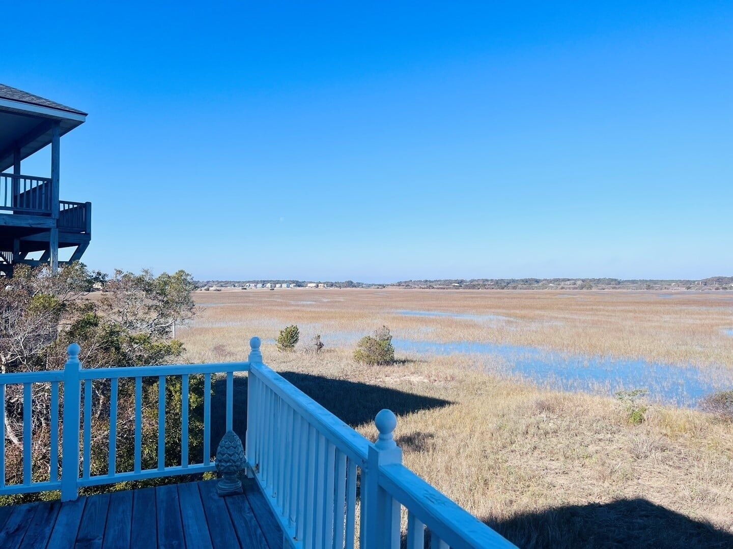 A wooden deck with a railing overlooking a flat landscape with sparse vegetation and a clear sky.