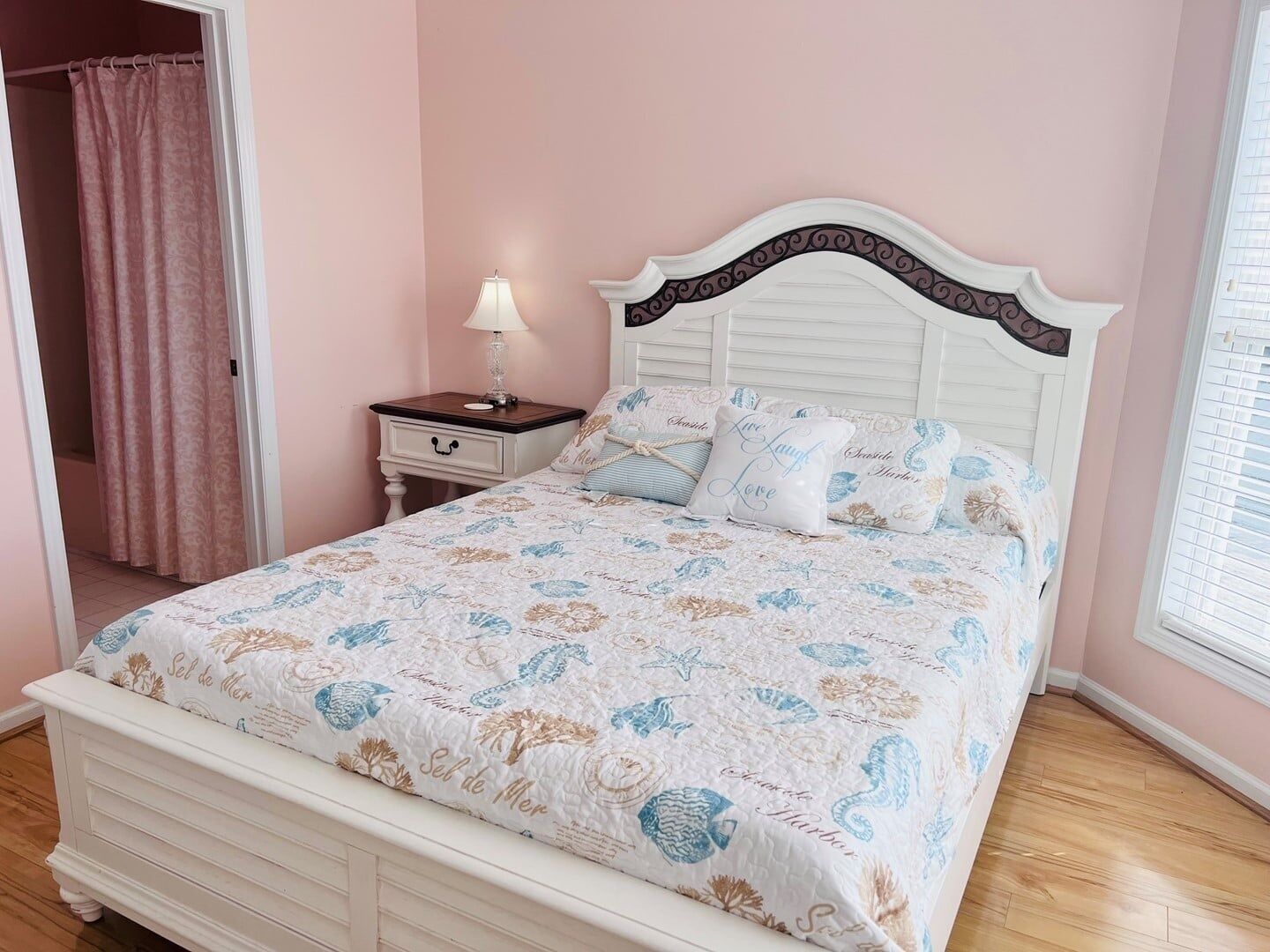 A bedroom with a bed, a nightstand, a lamp, and a window with blinds.
