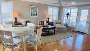 A spacious living room with a glass-top dining table, white wicker chairs, a sofa, a coffee table, and a ceiling fan. - Victoria - 3 Br Home (Supply)