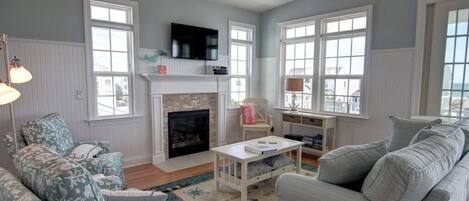 A living room with a fireplace, a ceiling fan, and large windows.