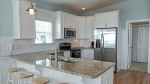 A kitchen with white cabinets, a granite countertop, a stainless steel refrigerator, and a microwave. - Welcome  4 Bedroom Home by RedAwning (Supply)