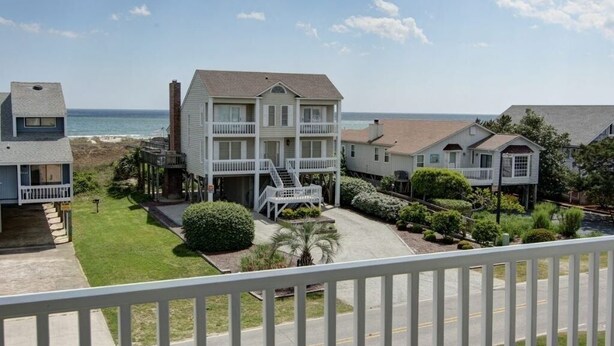 A beachfront property with multiple-story buildings, a well-maintained lawn, and a clear view of the ocean. - Welcome  4 Bedroom Home by RedAwning (Supply)
