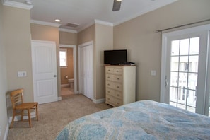 A bedroom with a bed, a dresser, a television, and a door leading to a balcony.
