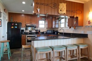 Une cuisine avec des meubles de rangement en bois, un réfrigérateur noir, un îlot central avec des tabourets et des éléments décoratifs sur le mur.