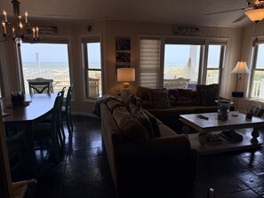 A cozy living room with a view of the ocean, a dining area with chairs, a sofa, and a table with a lamp.