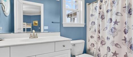 Un baño con tocador blanco, inodoro y cortina de ducha con motivos marinos.