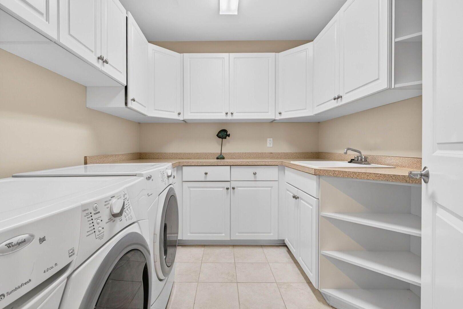 A laundry room with a front-loading washer and dryer, white cabinetry, a countertop with a sink, and a small green decorative item on the wall.