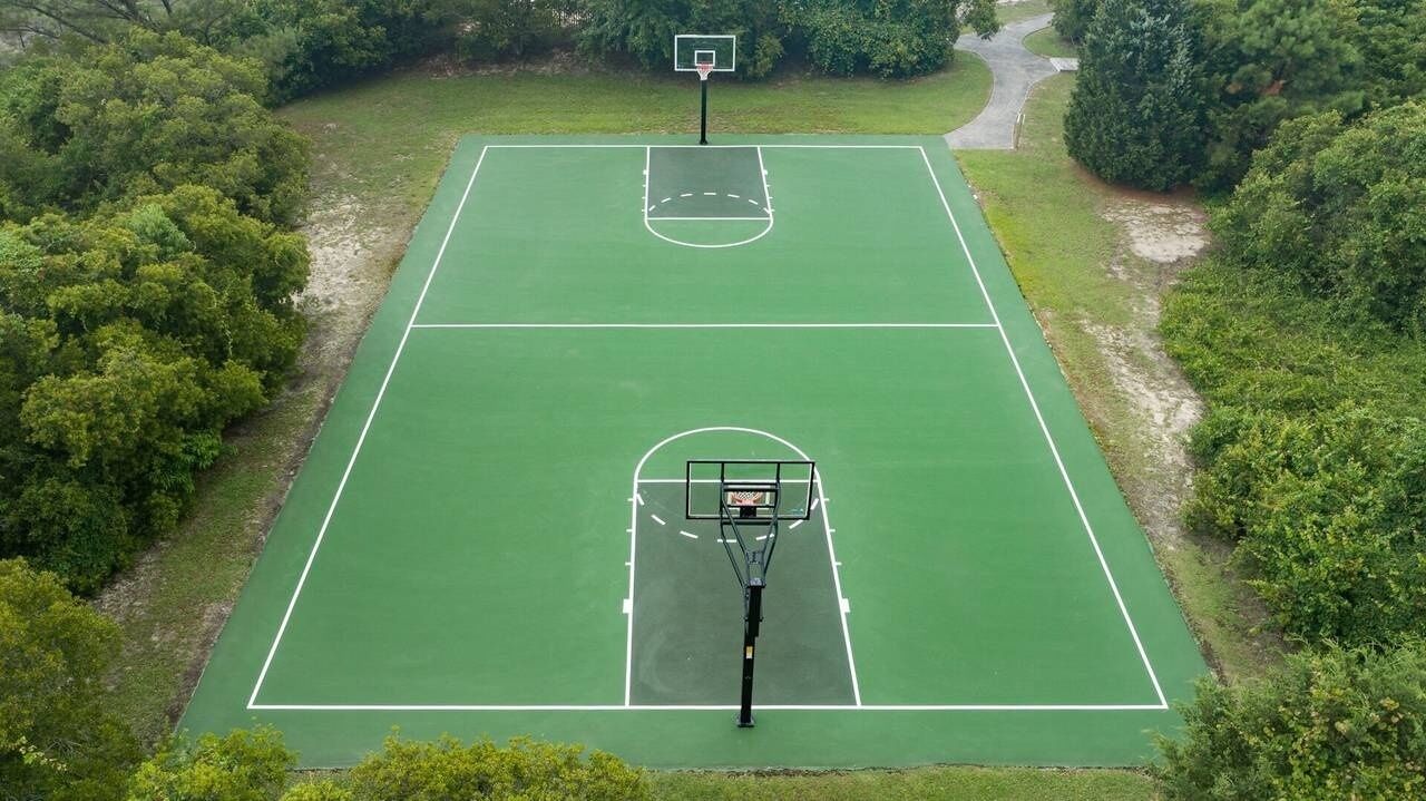 An aerial view of a basketball court with two hoops, surrounded by trees.