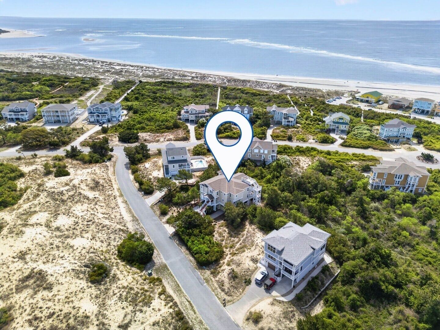 Luchtbeeld van een kustbewoonbaar gebied met meerdere tweelaagse huizen, een weg en een strand op de achtergrond.