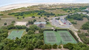 Ett flygbildsbild av ett kustnära område med två tennisbanor, en parkeringsplats och en byggnad med ett sluttande tak.