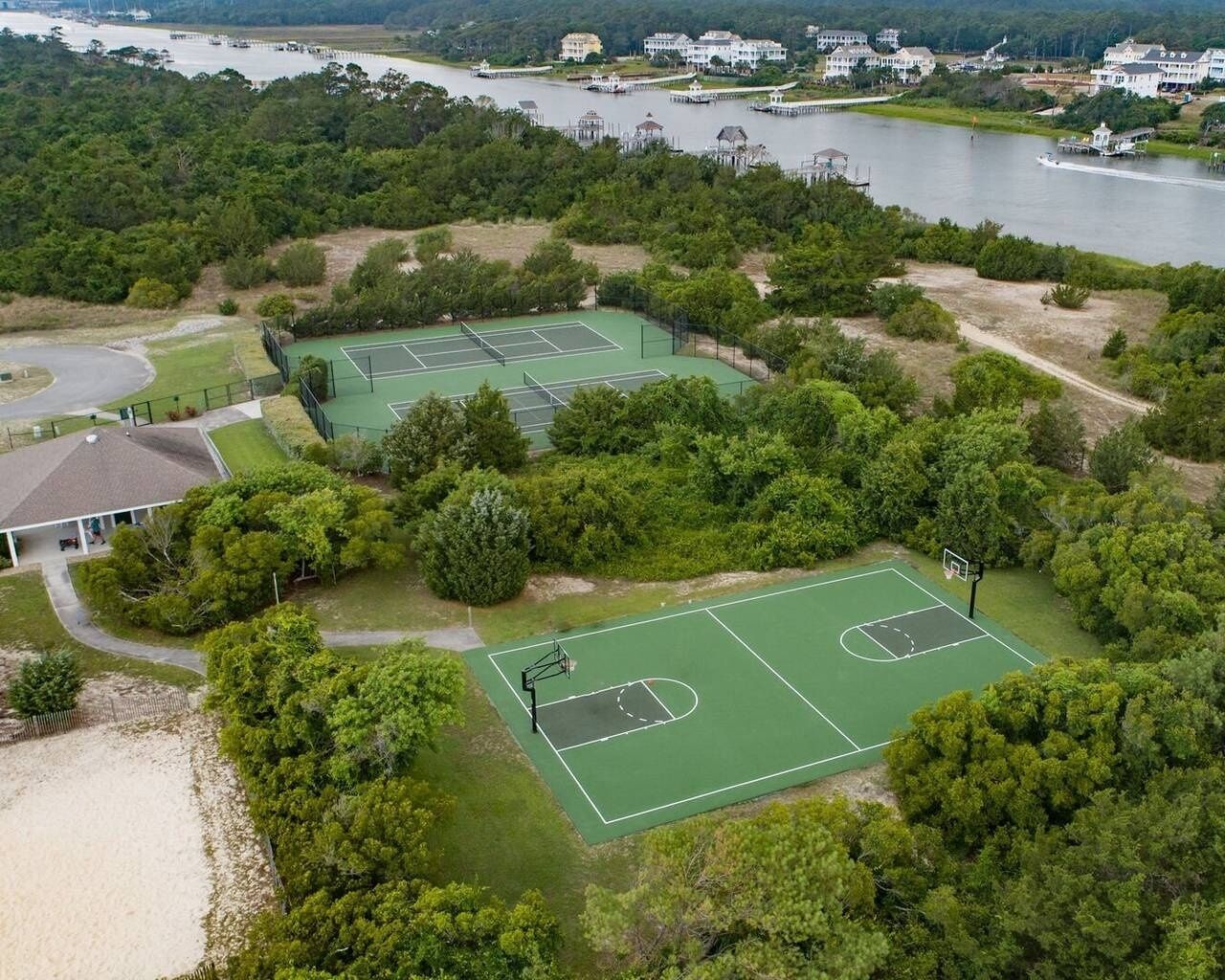 Una vista aerea di un campo da tennis circondato da vegetazione lussureggiante e un'area d'acqua.