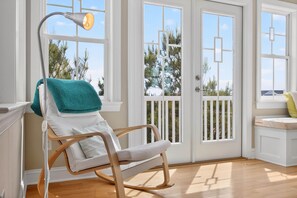 A room with a rocking chair, a desk, and a window with a view of trees.