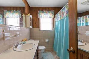 Un baño con paneles de madera, inodoro, lavabo y cortina de ducha.