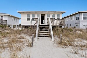 A beachfront property with a wooden staircase leading to a house with a balcony.